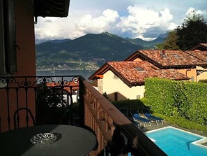 Un balcón con vistas a montañas, una piscina y una mesa con un vaso.