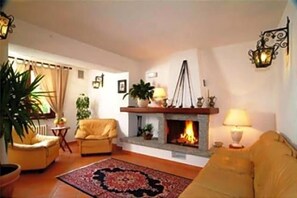 A living room with a fireplace, yellow sofas, a patterned rug, and a potted plant. - Hotel Adler (Menaggio)
