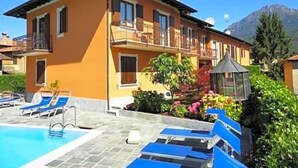 A two-story building with a swimming pool, lounge chairs, and a garden area. - Hotel Adler (Menaggio)
