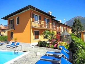 A two-story building with a swimming pool, lounge chairs, and a garden area. - Hotel Adler (Menaggio)