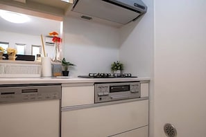 A kitchen with a dishwasher, stove, and a small potted plant. - Coco Shinjuku Hotel (Tokyo)