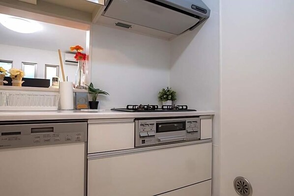 A kitchen with a dishwasher, stove, and a small potted plant. - Coco Shinjuku Hotel (Tokyo)