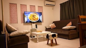 A living room with a sofa, a coffee table, a TV, and a small stool. - Coco Shinjuku Hotel (Tokyo)