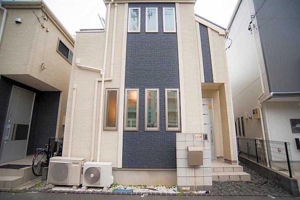 A modern two-story residential building with a central dark brick facade, multiple windows, and a small front porch.