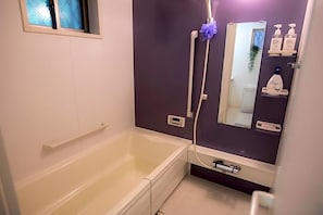 A bathroom with a bathtub, a shower, a mirror, and toiletries on a shelf. - Coco Shinjuku Hotel (Tokyo)