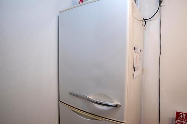 Un refrigerador blanco con manija plateada, un detector de incendios instalado en la pared y un enchufe.