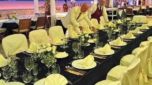 Una larga mesa de comedor dispuesta para un evento formal, con sillas cubiertas de tela amarilla, colocadas en fila.