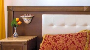 Un dormitorio con cabecera capitonada, una mesita de noche con un florero y una colcha estampada.