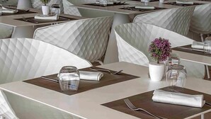 Un restaurante con mesas y sillas blancas, impecablemente preparadas con cubiertos y servilletas.
