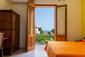 Quarto com cama, guarda-roupa e varanda com vista para o mar.