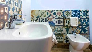 A bathroom with a white sink, bidet, and patterned tiles. - Hotel Egitarso Sul Mare (San Vito Lo Capo)