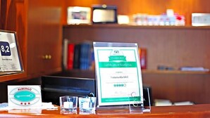 Una recepción de hotel con un certificado enmarcado, un letrero con el número de habitación 8,2 y una vitrina de cristal con una llave y un certificado.