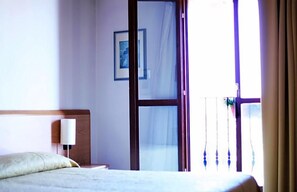A hotel room with a bed, a nightstand, a lamp, a framed picture on the wall, and a sliding glass door leading to a balcony. - Hotel Alla Nave (Masi)
