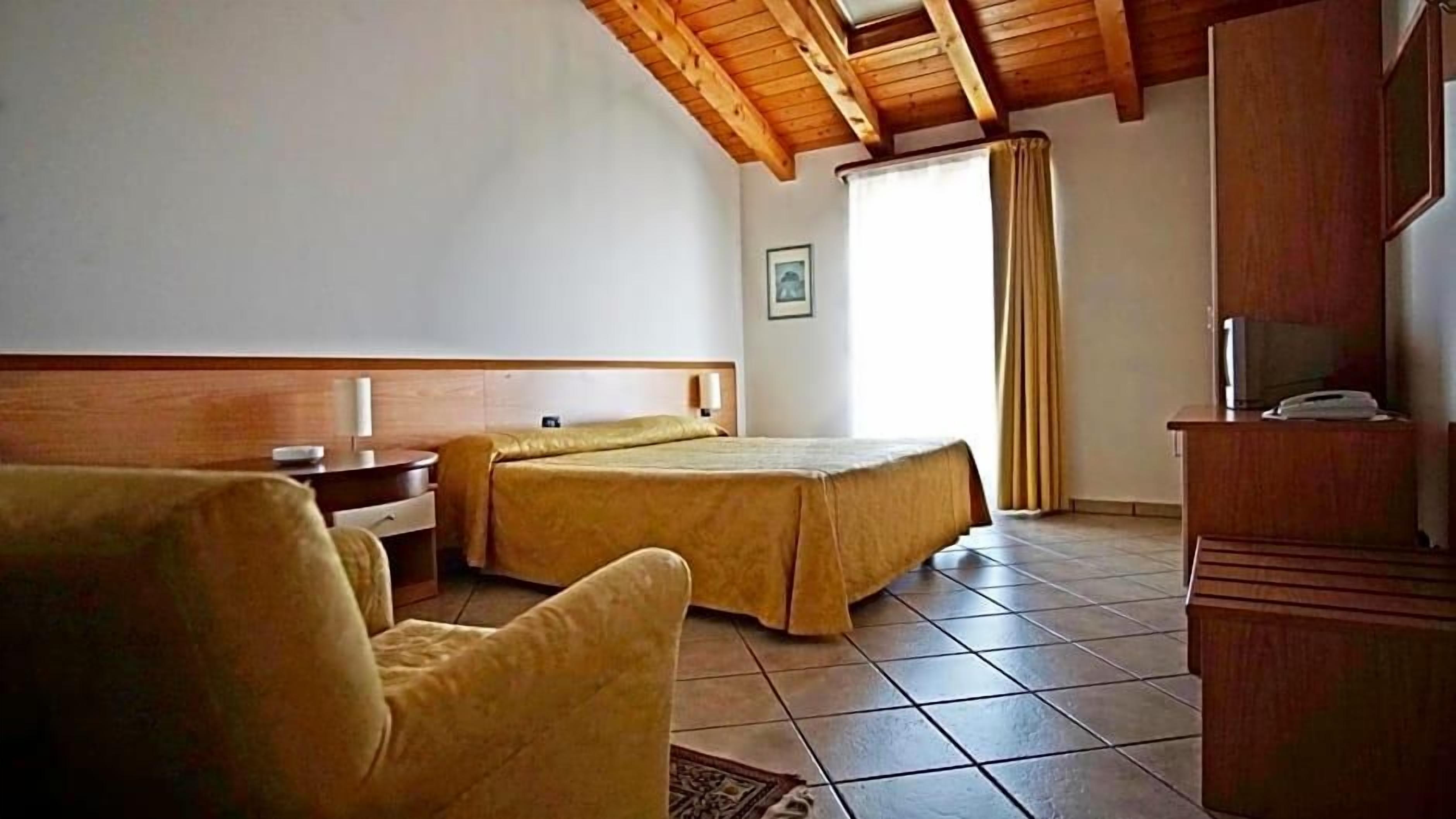 A hotel room with two beds, a desk, a chair, a television, and a window with curtains.