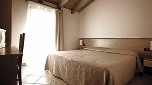 A hotel room with a bed, a desk, a chair, a nightstand, and a window with curtains. - Hotel Alla Nave (Masi)