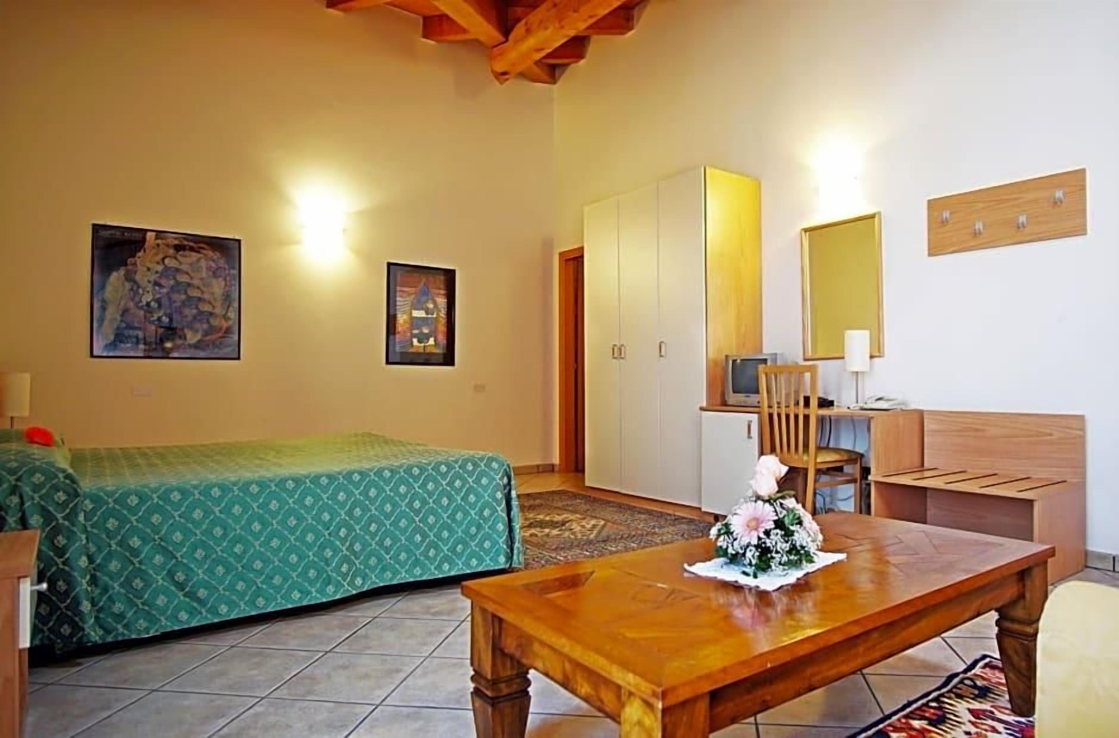 Quarto com cama, mesa de madeira com arranjo de flores, cadeira, guarda-roupa e espelho na parede.
