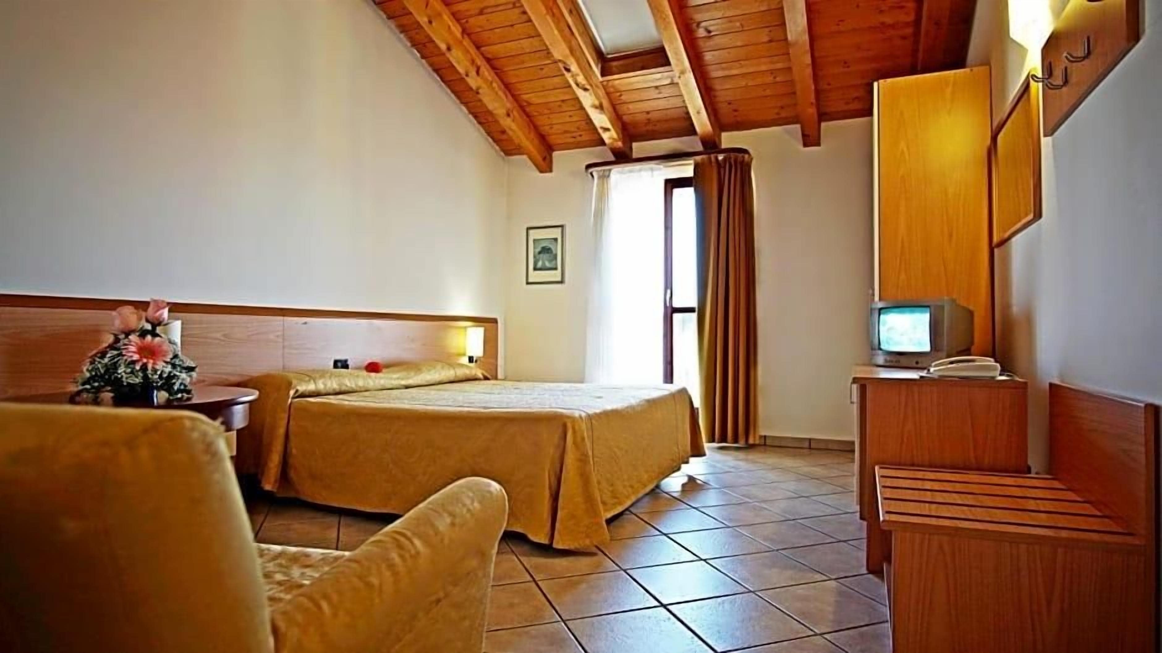 Una camera d'albergo con soffitto in legno, un letto con testiera, una televisione, una scrivania con telefono e una sedia.