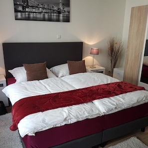 A hotel room with a large bed, a nightstand, a lamp, and a cityscape painting on the wall. - Hotel Eigelstein (Cologne)