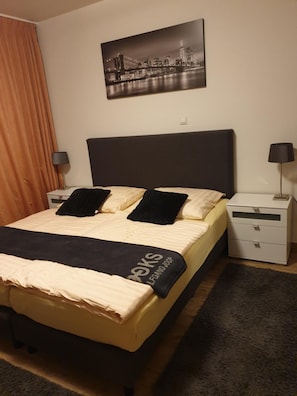 A hotel room with a bed, a nightstand, a lamp, a picture on the wall, and a window with curtains. - Hotel Eigelstein (Cologne)