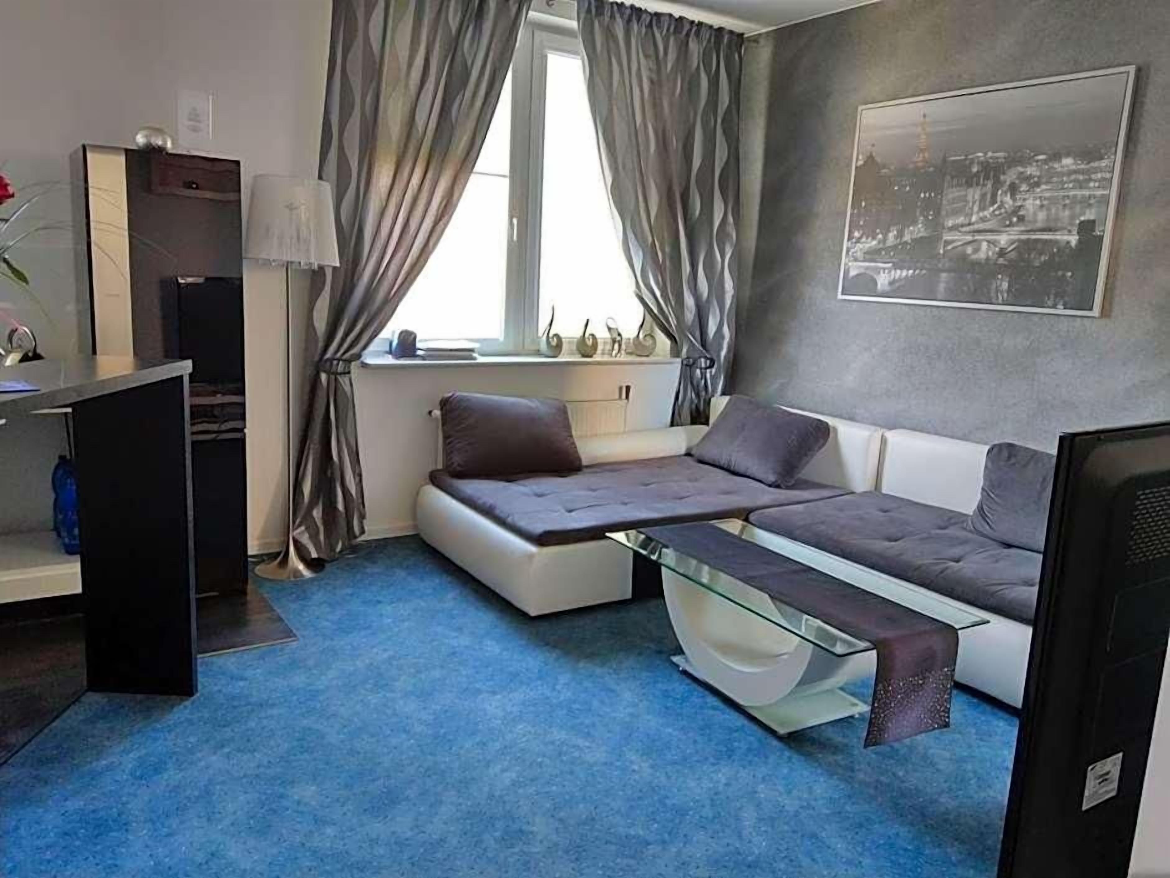 Habitación compacta con sofá cama, escritorio, silla, televisor y ventana con cortinas.