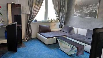 A compact room with a sofa bed, a desk, a chair, a TV, and a window with curtains.