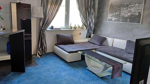 A compact room with a sofa bed, a desk, a chair, a TV, and a window with curtains.