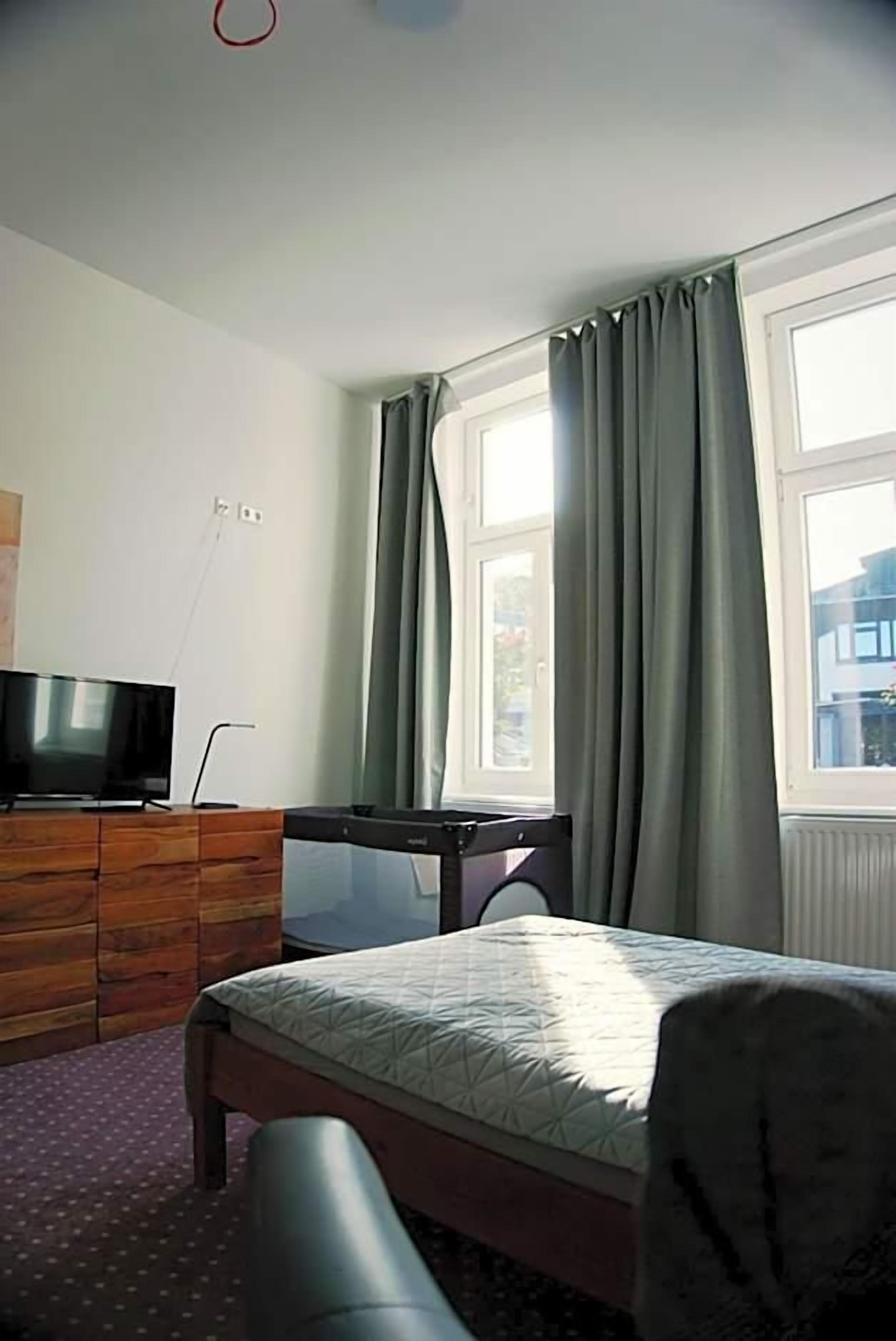 Ein Schlafzimmer mit einem Bett, einem Schreibtisch, einem Fernseher und einem Fenster mit Vorhängen.