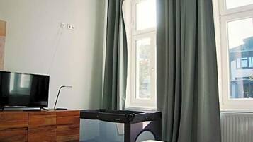 Ein Schlafzimmer mit einem Bett, einem Schreibtisch, einem Fernseher und einem Fenster mit Vorhängen.