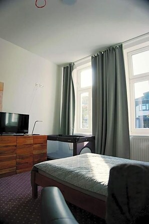 Un dormitorio con cama, escritorio, televisor y ventana con cortinas.