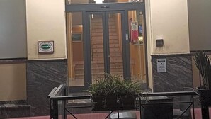 A hotel entrance with a sign reading 'HOTEL POSTA' and a star symbol. There is a door with a glass panel, a small sign on the wall, and a potted plant in front. - Hotel Posta (Ventimiglia)