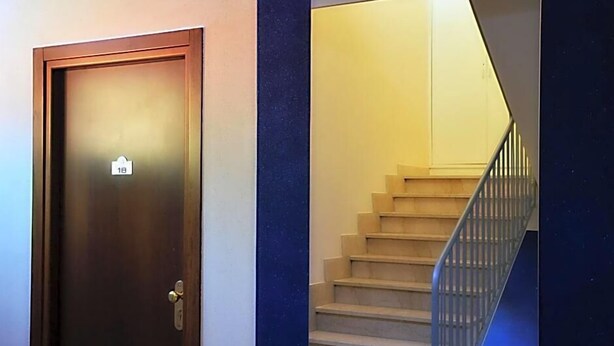 A wooden door with a number plate, a staircase with a metal railing, and a blue accent wall. - Hotel Posta (Ventimiglia)