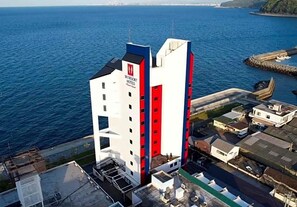 Un hotel con una fachada roja y blanca destacada, situado junto al mar y con vistas al océano.