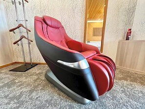 Una silla de masajes con base metálica y tapicería roja en una habitación con papel tapiz estampado y una puerta de madera.