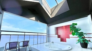 Un baño moderno con un ventanal grande, una bañera, una silla y una planta en maceta.