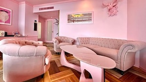 Habitación decorada en tonos rosas, con un sofá, sillones y una mesa de centro de vidrio.