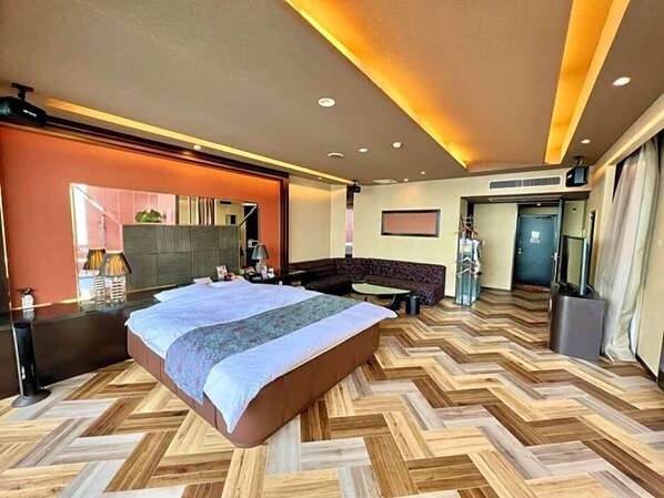 Hotellihuone, jossa on suuri sänky, sohva, työpöytä ja peili.