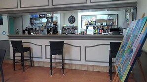 A bar area with two black bar stools, a clock, shelves with bottles, and a painting on the wall. - Le Lion D Or (Bernay)