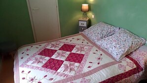 A bed with a floral-patterned quilt and a pillow, a bedside lamp, and a closed door. - Le Lion D Or (Bernay)