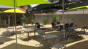An outdoor patio with tables and chairs under umbrellas, a stone wall, and potted plants. - Le Lion D Or (Bernay)