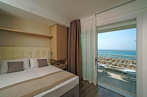 A hotel room with a large bed, a nightstand, a wardrobe, and a balcony with a view of the beach and ocean. - Hotel Strand A Frontemare (Jesolo)