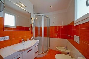 Ein Badezimmer mit Dusche, Waschbecken und Toilette, ausgestattet mit einer Duschkabine aus gebogenem Glas und einem weißen Waschtisch.