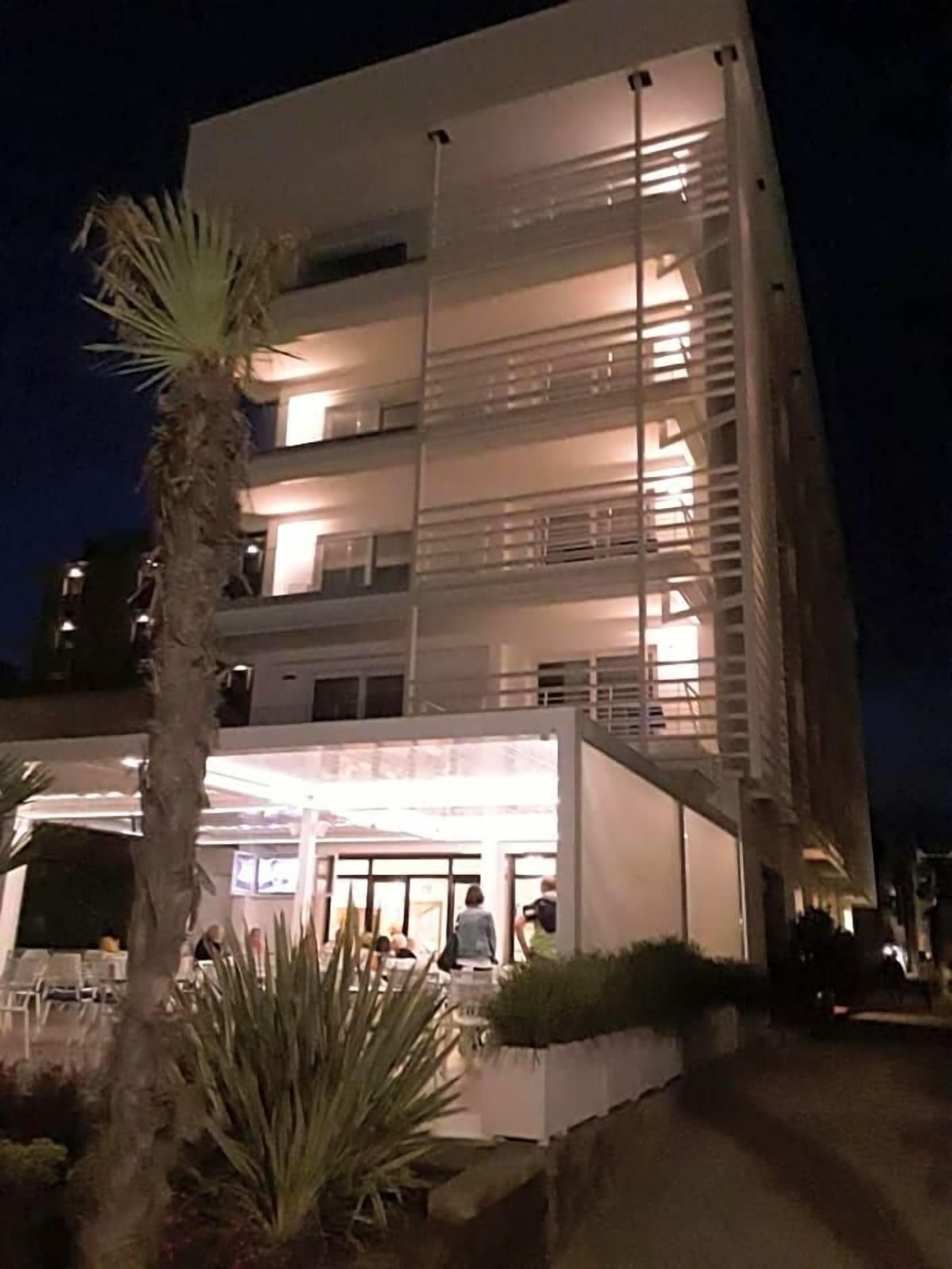 A multi-story hotel with balconies, a covered outdoor area, and a palm tree.