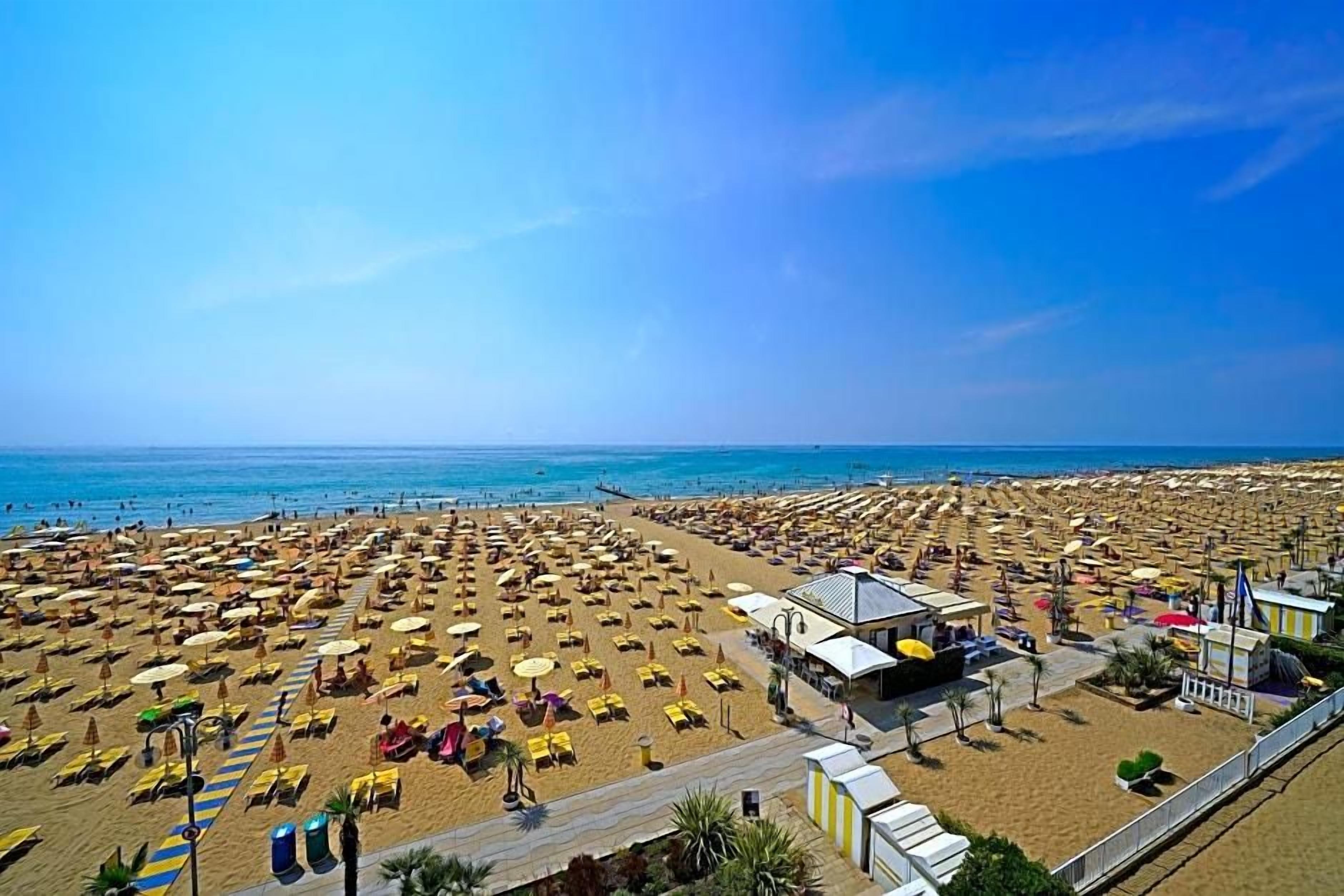 A beach with rows of sunbeds and umbrellas, a lifeguard tower, and a boardwalk.