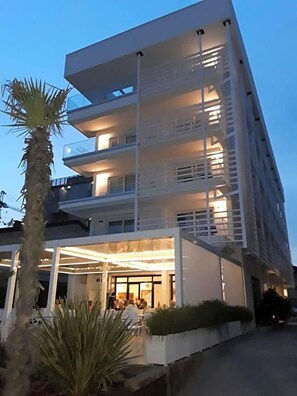 A multi-story hotel with balconies, outdoor seating, and a palm tree. - Hotel Strand A Frontemare (Jesolo)