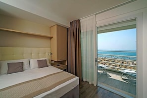 A hotel room with a large bed, a nightstand, a wardrobe, and a balcony with a view of the beach and ocean. - Hotel Strand A Frontemare (Jesolo)