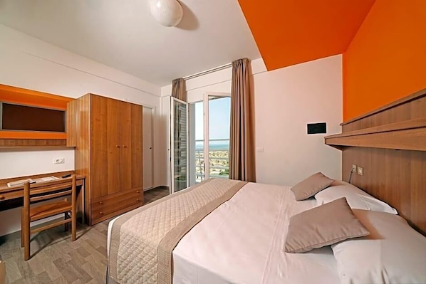 Ein Hotelzimmer mit Bett, Schreibtisch, Kleiderschrank und einer Glastür zum Balkon.