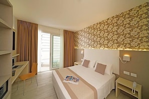Ein Hotelzimmer mit einem Bett, einem Schreibtisch, einem Stuhl, einem Nachttisch und einer Wand mit einem Blumenmuster.