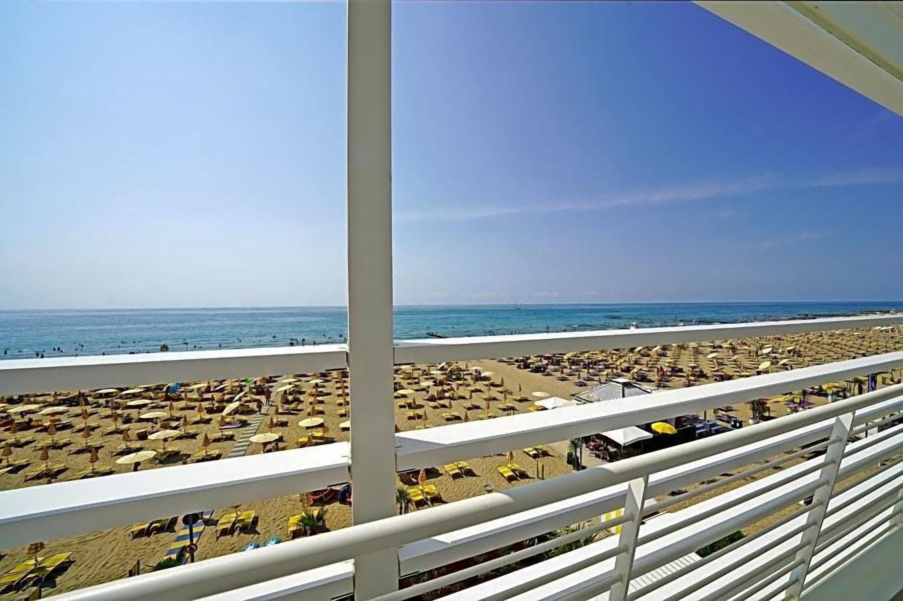 A beach view with rows of sun loungers and umbrellas, a clear sky, and the ocean in the background.