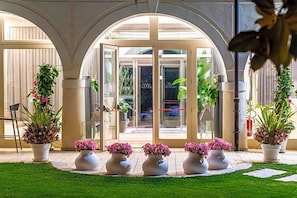 A hotel entrance with a glass door, potted plants, and a well-maintained lawn. - Villa I Pini (Civitella in Val di Chiana)