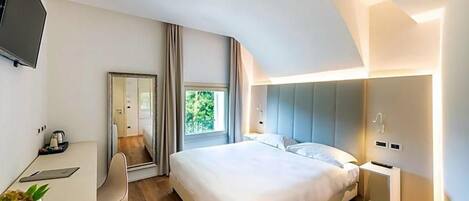 A modern hotel room with a large bed, a desk with a chair, a TV, and a window with curtains.